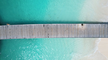 Wooden pier dividing turquoise water and white sand beachの写真素材