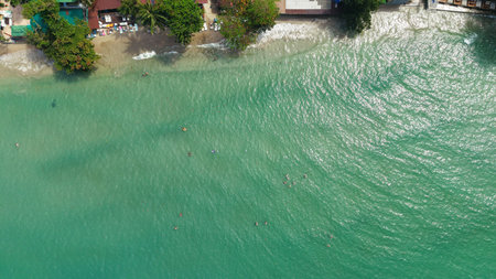 Tourists swimming in tropical emerald green water near sandy beach with resort, aerial viewの写真素材