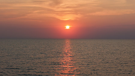 Bright red sunset reflecting on calm ocean watersの写真素材
