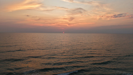 Sunset painting the ocean with warm hues and wispy cloudsの写真素材