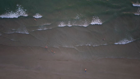 Tourists enjoying relaxing swim in ocean waves on sandy beachの写真素材