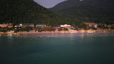 Tioman island glowing with lights at dusk, tranquil coastal scene from aboveの写真素材