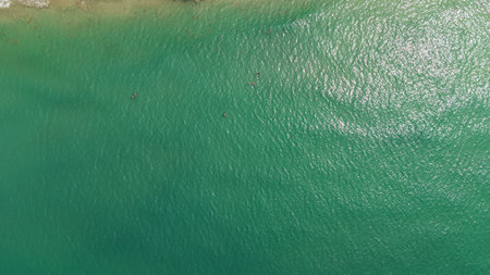 Turquoise water surface reflecting sunlight with people swimming in the distanceの写真素材