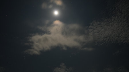 Bright moon shining through clouds in starry night skyの写真素材