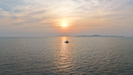 Boat sailing towards sunset over calm ocean with island in backgroundの写真素材