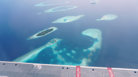 Airplane wing flying over maldives islands and atolls in the indian ocean