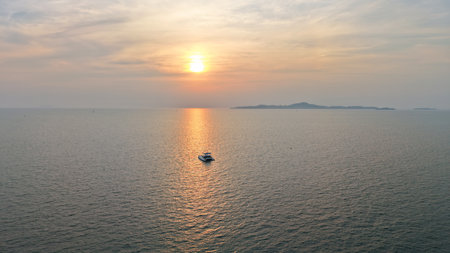Catamaran sailing towards sunset over calm ocean with island in backgroundの写真素材