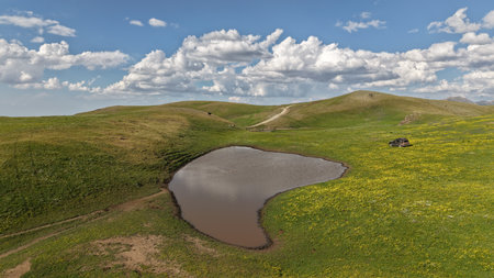 Small pond reflecting clouds in green landscape with suv carの写真素材