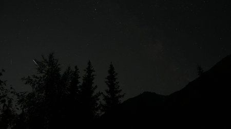 Northern lights glowing faintly over mountain forest silhouettesの写真素材