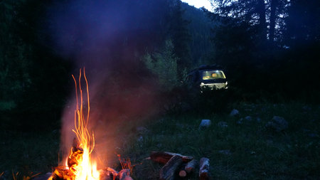 Campfire burning brightly in wilderness with off road vehicle in backgroundの写真素材