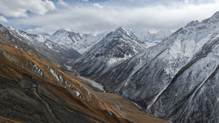 Majestic snow-capped mountains with valley and river under cloudy sky