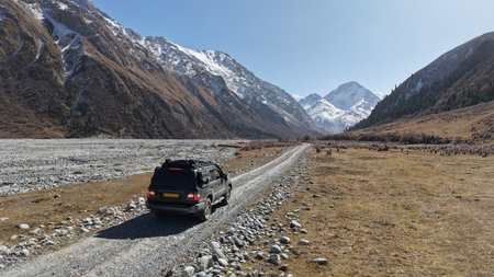 SUV driving on gravel road through mountainous landscape with clear skyの写真素材