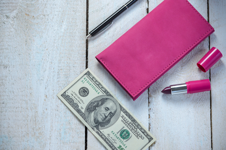 Workplace with pink leather wallet, money, pen and lipstick on white wooden table. Flat compositionの写真素材