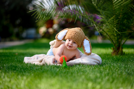 Baby in the hat like a bunny with carrot toy on green grass outdoorsの写真素材