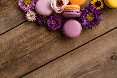 Violet and yellow macarons and flowers on wooden table background. Colorful french dessert with fresh flowers. Autumn conceptの写真素材