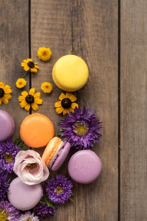 Colorful Macarons and flowers on wooden table background. French dessert with fresh flowers. Top view. Autumn conceptの写真素材