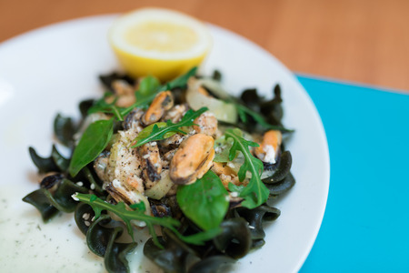 Black pasta with seafood in white cream sauce and lemon. Blue backgroundの写真素材