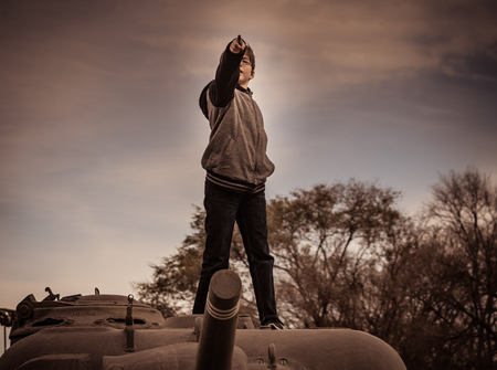 Playing war games on top of an antique Army tank, the boy pretends to lead his army into battle.の写真素材