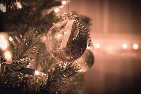 A pretty silver Christmas ornament with ribbon and beads, hangs from a Christmas tree against a dreamy background with soft warm light and bokeh.の写真素材