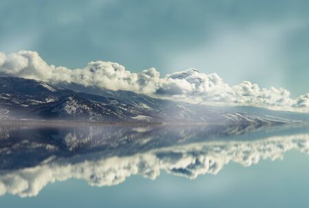 A mountain lined with clouds reflects in the adjacent lake, as a flock of birds fly above the water. This is a digital creation I made from a photo I took of the mountains just after the season's first dusting of snow.の写真素材