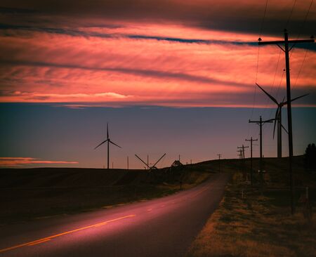 A beautiful cloudy sunset reflects on a country road surrounded by farm fields and wind turbines in rural Idaho.の写真素材