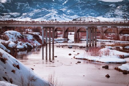 The Bear River Dam in Grace, Idaho in winter. Sun sets on still and shallow water surrounded by snow-covered cliffs and mountains in this rural Idaho scene.の写真素材