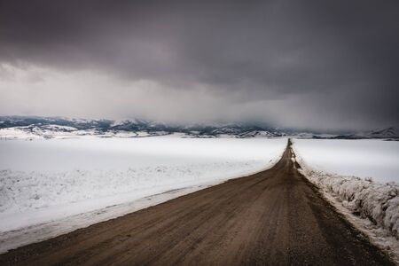 Dark storm clouds roll in over this dirt country road that runs down the middle of a snow-covered field in rural Idaho.の写真素材