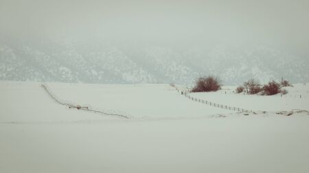 A crop irrigation system sits on a snow-covered field in winter. Fog blankets the mountainside, as wind blowing snow causes near whiteout conditions in a rural Idaho location.の写真素材