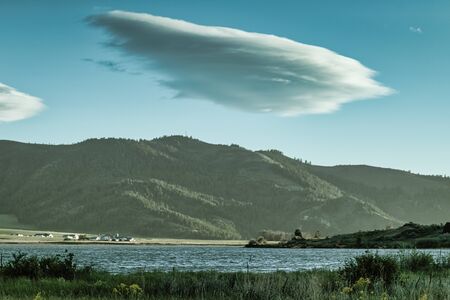 A large swirling cloud hovers above the  blue Alexander Reservoir and forest covered mountains in Idaho.の写真素材