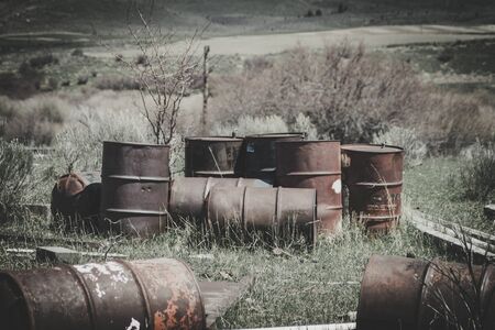A bunch of old rusty barrels sit abandoned in a field. Some bullet holes can be seen from people shooting at them. The overall image gives off a vintage urbex vibe.の写真素材