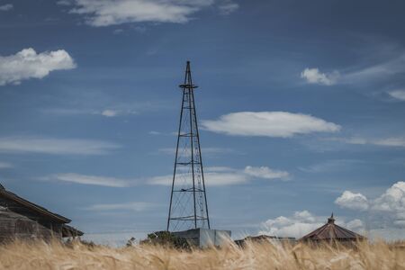 A vintage broken windmill tower sits on an abandoned rural farm and golden grain field.の写真素材