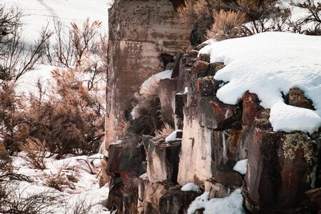 Snow sits on top of colorful lava rocks that form this cliff. Dried sagebrush pokes through snow and rocks, lending to this chilly scene.の写真素材