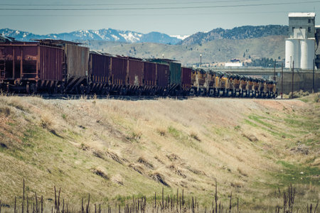 A train with grain hopper cars is being pulled by several engines as it approaches a grain silo near...