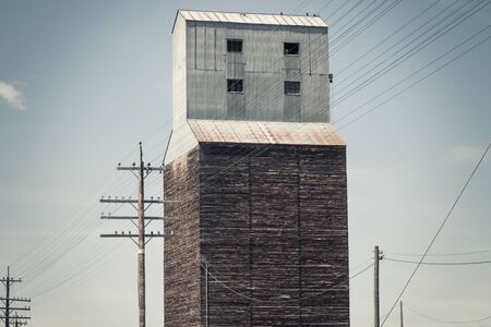 An old grain elevator in Soda Springs, ID sits abandoned next to railroad tracks and a blue sky. Surrounded by electrical wires and poles, this grain elevator is an iconic part of the Soda Springs skyline and it`s rich farming and shipping history.の写真素材