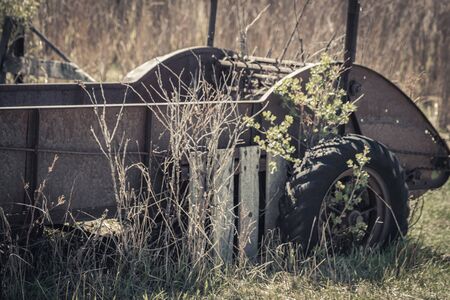 An old vintage hay baler cart sits in a field surrounded by grass and bushes. It is now being used as lawn decor and a flower planter.の写真素材