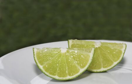 Two wedges of lime on a white plate, green backgroundの写真素材