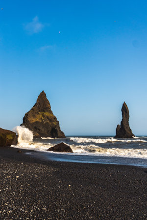 The dramatic Reynisfjara Beach features black volcanic sands and towering basalt sea stacks rising from the wild Atlantic Ocean in Icelandの写真素材