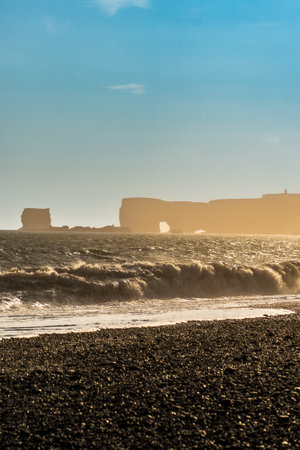 The dramatic Reynisfjara Beach features black volcanic sands and towering basalt sea stacks rising from the wild Atlantic Ocean in Icelandの写真素材