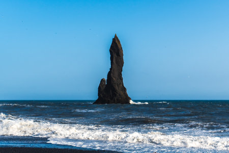 The dramatic Reynisfjara Beach features black volcanic sands and towering basalt sea stacks rising from the wild Atlantic Ocean in Icelandの写真素材