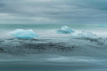A breathtaking view of JÃ¶kulsÃ¡rlÃ³n Glacier Lagoon with floating icebergs and the contrasting black sands of Diamond Beach in Iceland, under a dramatic sky.の写真素材