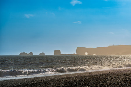 The dramatic Reynisfjara Beach features black volcanic sands and towering basalt sea stacks rising from the wild Atlantic Ocean in Icelandの写真素材