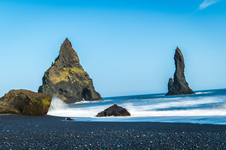 The dramatic Reynisfjara Beach features black volcanic sands and towering basalt sea stacks rising from the wild Atlantic Ocean in Icelandの写真素材