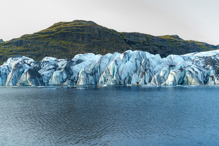 SÃ³lheimajÃ¶kull Glacier stretches down from the mountains into a serene lake, showcasing Iceland's stunning icy landscapeの写真素材