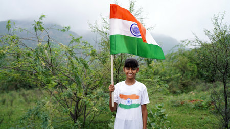 Cute Indian girl holding Indian flag in her hand and smiling. Celebrating Independence day or Republic day in India. A girl showing pride of Tiranga. Har Ghar Tirangaの写真素材