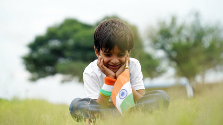 Happy Indian Cute Smiling little boy waving tricolor flag at outdoor park, celebrating Independence...