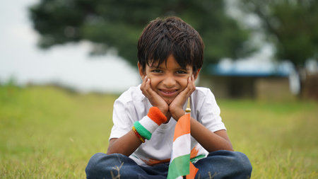 Happy Indian Cute Smiling little boy waving tricolor flag at outdoor park, celebrating Independence...