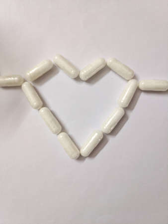 White pills in the shape of cardiography near white plastic bottle on red table. Concept of heart diseases, problems with heartの写真素材