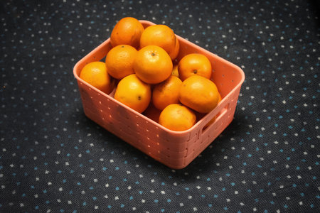 A wicker basket full of fresh orange fruits, isolated on a blue and white dotted...
