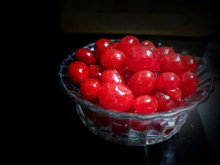 Metallic vintage tray, surface and cup with red juicy cherries inside the cup and scattered around the tray with black background, selective focusの写真素材
