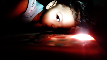 Cute little girl playing with a flashlight in a dark room.の写真素材